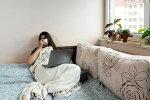 Vrouw ziek thuis met laptop, zoekt ziekte-uitkering.